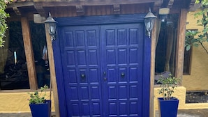 Une porte bleue à deux battants, donnant sur une entrée pavée de pierres.