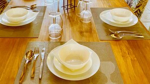 Une table à manger dressée pour un repas, avec des chaises, des assiettes, des couverts et des verres à vin.