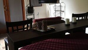 Una habitación con una cama, un televisor montado en la pared, una mesa de comedor con sillas y una mesita con velas.