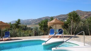 Ein Swimmingpool mit blauem Wasser, umgeben von Liegestühlen und einem Strohdachschirm.