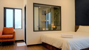 Une chambre d’hôtel avec un lit, une chaise, une grande fenêtre et un espace douche.