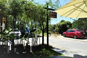 A roadside view of Oasis Hotel with a signboard, potted plants, and a red car parked nearby.