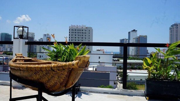 Une terrasse sur le toit, agrémentée d’un jardinière en osier tressé, d’un lampadaire et, en arrière-plan, d’une vue sur les toits de la ville.