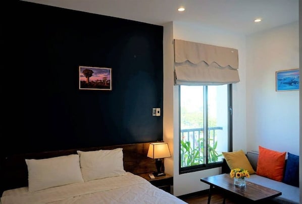 A bedroom with a bed, bedside lamp, window with curtains, and a small table with a vase of flowers.