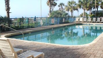 A swimming pool with lounge chairs and palm trees, surrounded by a fence.