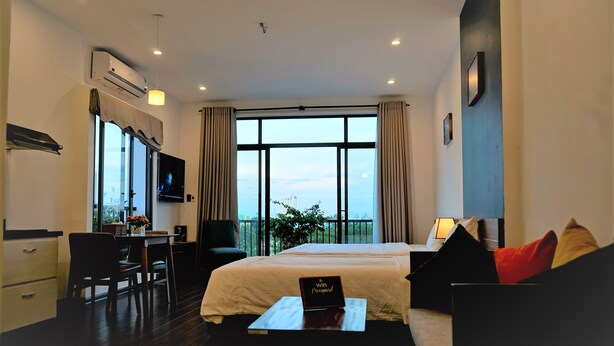 Quarto de hotel com cama, escrivaninha, cadeira, ar condicionado, televisão e varanda com vista.