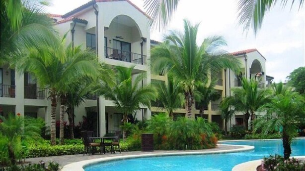 Un hotel con piscina rodeado de palmeras y un edificio de dos pisos con balcones.