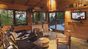 Un interior de cabaña acogedor con techo de madera, ventanas amplias, televisor y chimenea.
