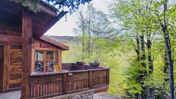Una cabaña de madera con balcón que da a un área boscosa.