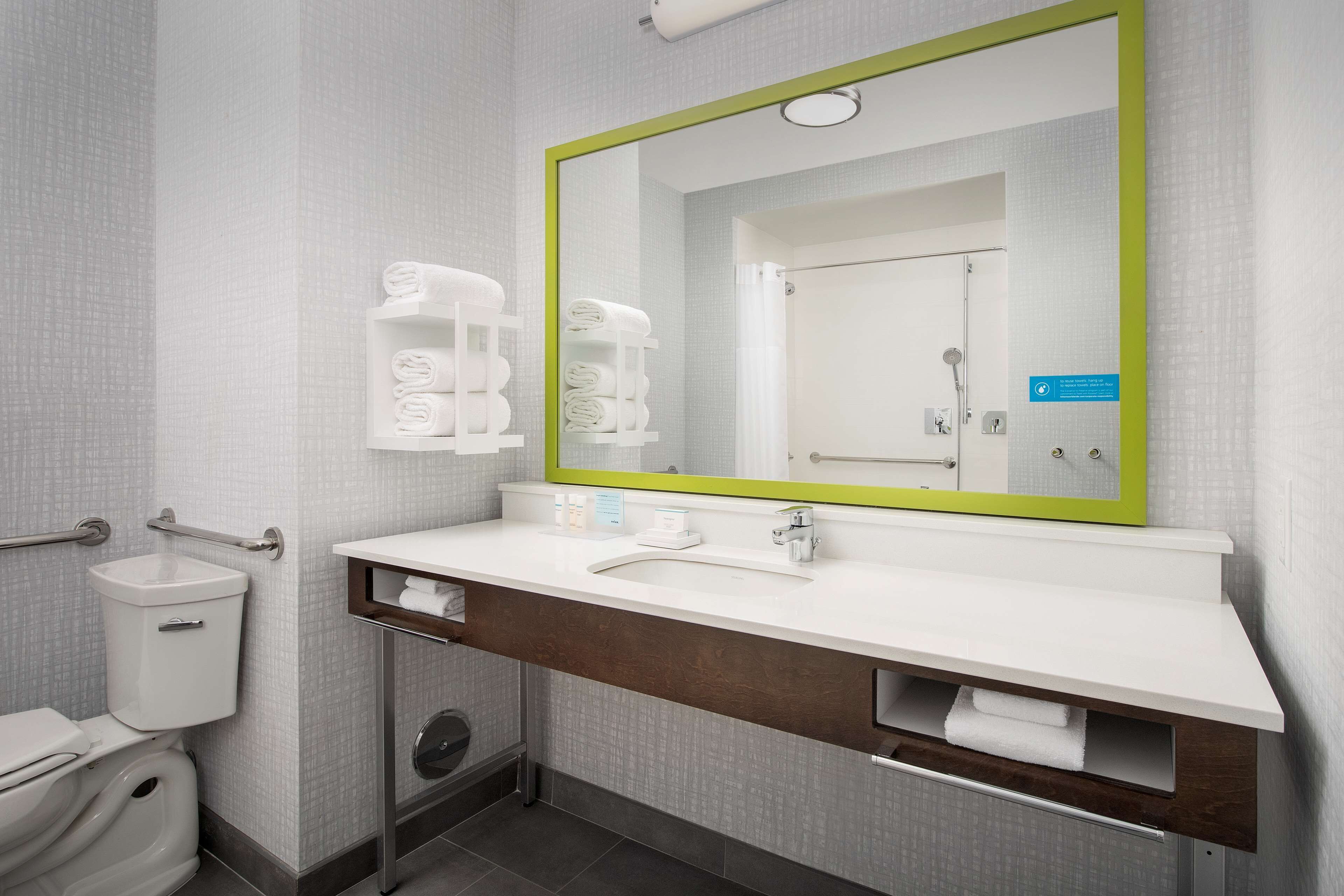 A modern bathroom with a white sink, a mirror with a green frame, and a toilet.