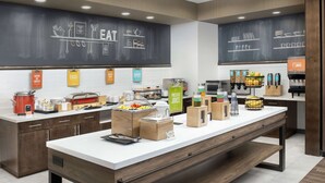 A modern kitchen area with a long counter, various food items, and a chalkboard with food-related drawings. - Hampton Inn & Suites Lexington Columbia (Lexington)