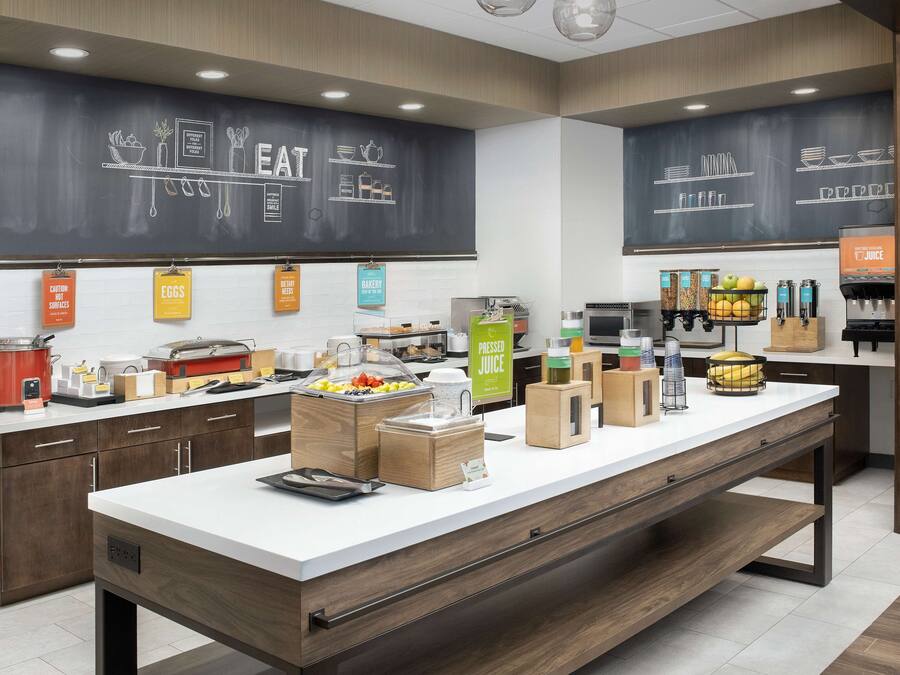 A modern kitchen area with a long counter, various food items, and a chalkboard with food-related drawings.