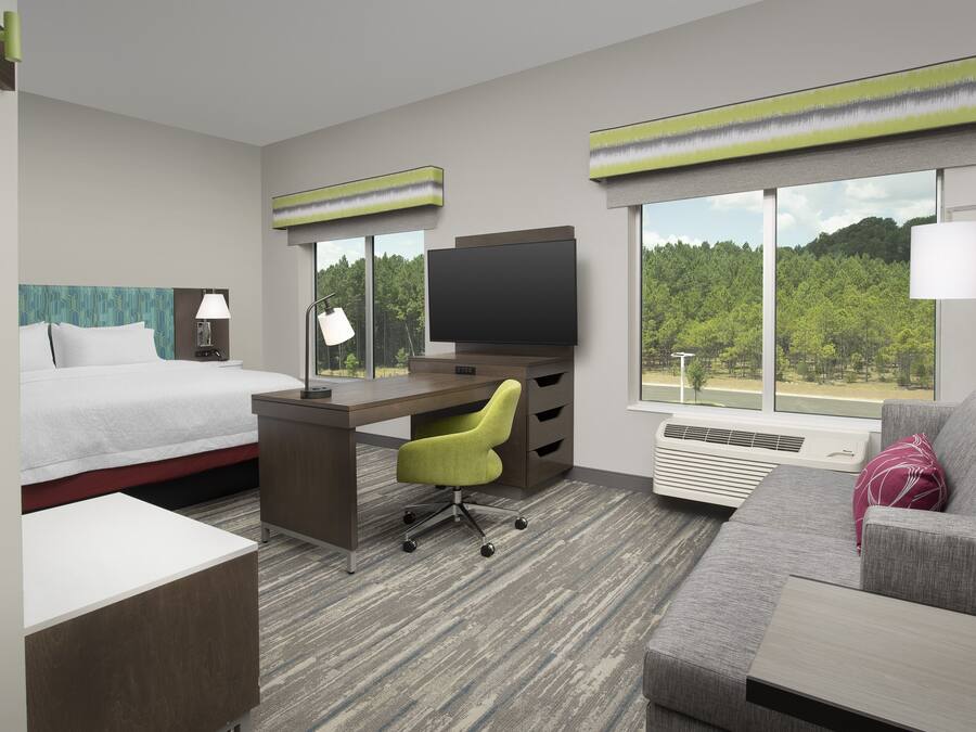 A hotel room with a bed, desk, chair, TV, and a sofa.