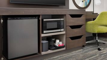 A compact kitchenette with a microwave, coffee maker, and storage drawers.