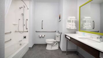 Un baño moderno con bañera, inodoro y lavamanos, equipado con barras de apoyo y una silla de ducha.