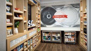 A snack and sundries section with wooden shelves stocked with various snacks and beverages, and a wall mural with a circular design. - Hampton Inn & Suites Lexington Columbia (Lexington)