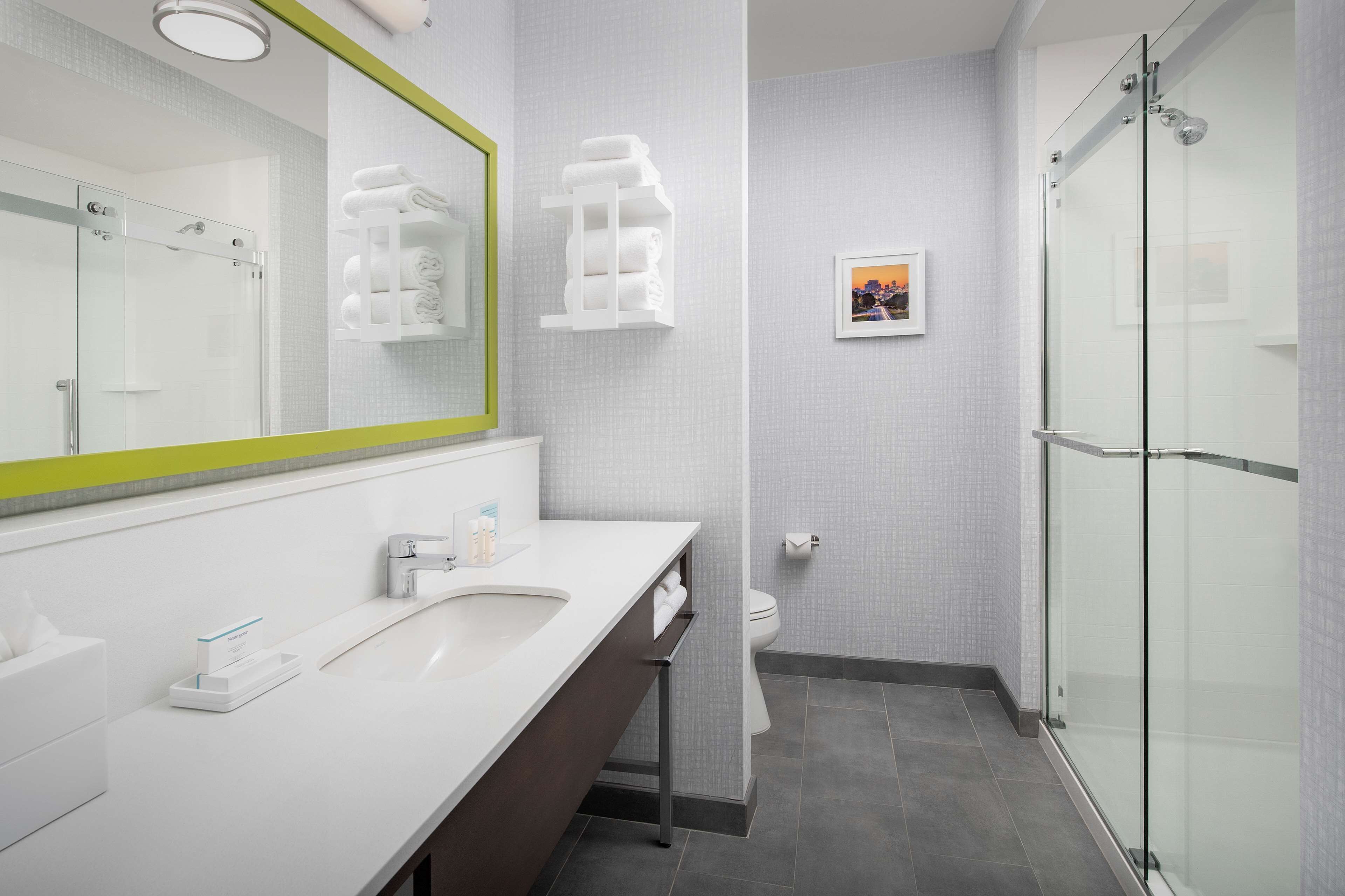 A modern bathroom with a large mirror, a sink, a toilet, and a glass-enclosed shower.
