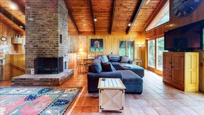 A cozy living room with a fireplace, wooden ceiling, and large windows.