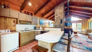 A rustic kitchen with wooden cabinets, a stone wall, and a large island with bar stools.