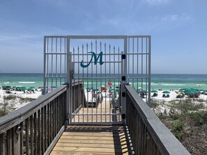 A wooden boardwalk leading to a beach with umbrellas and a gate with a 'M' sign. - Dog-friendly, 2 bed/2ba with beach service for 4, Miramar Beach, FL by Destin (Miramar Beach)