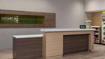 A reception desk with a sign reading "HOME 2 SUITES BY HILTON HONORS".