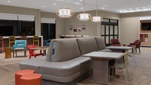 A modern lounge area with a grey sectional sofa, orange ottomans, and a wooden table. - Home2 suites by Hilton, Carlsbad, New Mexico (Carlsbad)