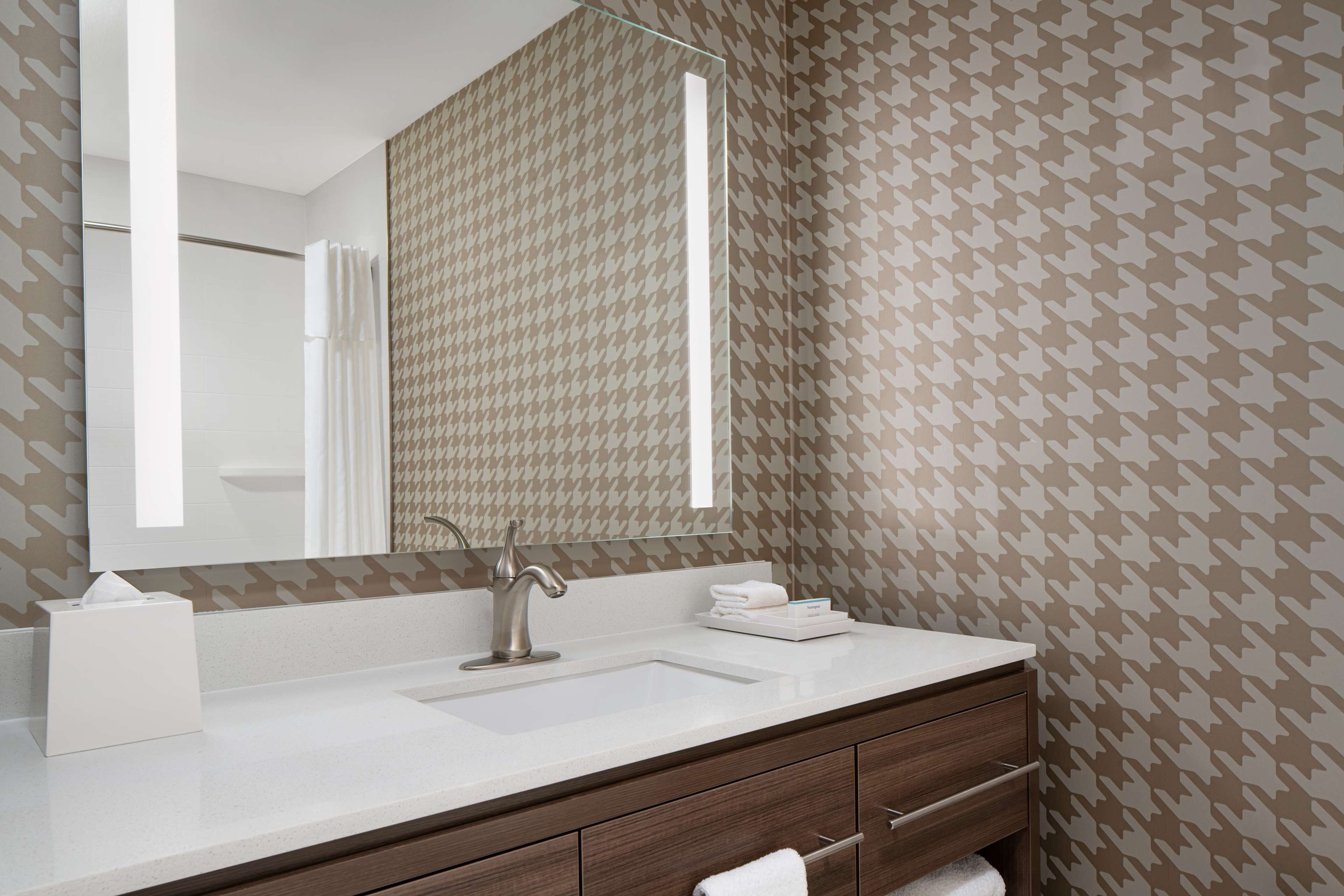 A bathroom with a large mirror, a sink, a towel rack, and a wooden vanity.