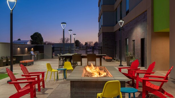 An outdoor patio with a fire pit, red and yellow chairs, and tables. - Home2 suites by Hilton, Carlsbad, New Mexico (Carlsbad)