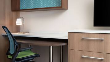 A modern office desk with a chair, a lamp, and a cabinet with drawers.