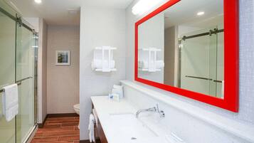 A modern bathroom with a glass shower enclosure, a white sink with a red-framed mirror, and a toilet.
