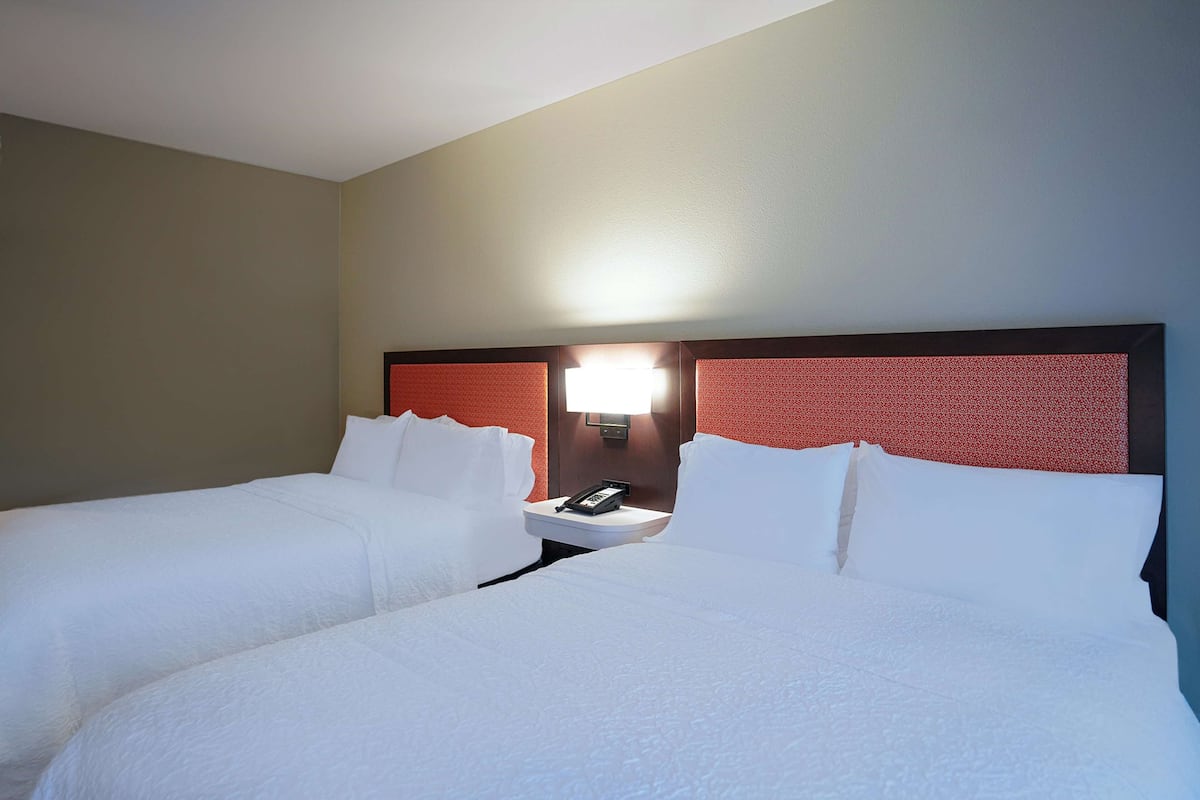A hotel room with two beds, a nightstand with a phone, and a wall-mounted light.