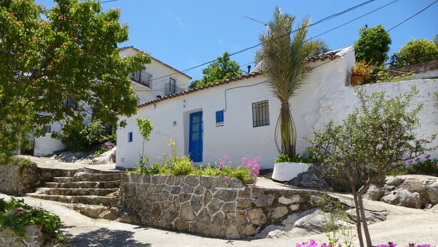 Un edificio blanco con puerta azul, escalones de piedra y plantas en macetas.
