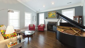 A living room with a grand piano, red armchairs, a glass coffee table, and a fireplace. - Luxury oasis with chef's dream kitchen and many outdoor spaces (Asheville)