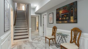 A hallway with a staircase, wooden chairs, a glass table, and a framed painting on the wall. - Luxury oasis with chef's dream kitchen and many outdoor spaces (Asheville)