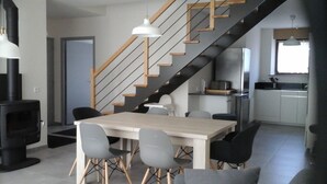 Una cocina moderna con una isla central, un comedor con mesa y sillas, y una escalera que conduce a un nivel superior.