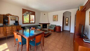 A spacious living area with a dining table, chairs, a sofa, and a fireplace. - Club Villamar - Nice and cozy villa with private pool, located in a quiet area with nice views (Macanet de la selva)