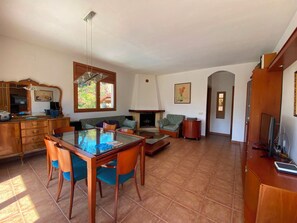 A spacious living area with a dining table, chairs, a sofa, and a fireplace. - Club Villamar - Nice and cozy villa with private pool, located in a quiet area with nice views (Macanet de la selva)