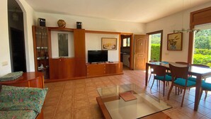 A spacious living area with a sofa, a coffee table, a TV, and a dining table with chairs. There is a kitchen visible through an open doorway. - Club Villamar - Nice and cozy villa with private pool, located in a quiet area with nice views (Macanet de la selva)