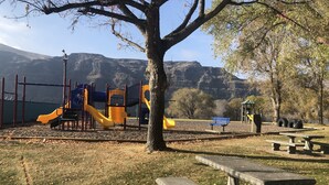 A park with a playground, picnic tables, and a bench.