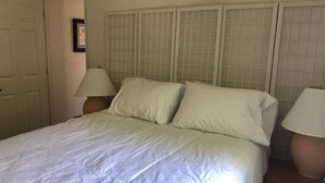 A bed with white bedding, two bedside tables with lamps, and a door in the background.