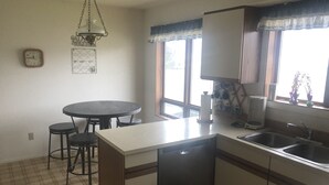 A kitchen with a dining table, two stools, a dishwasher, a coffee maker, and a window with curtains.