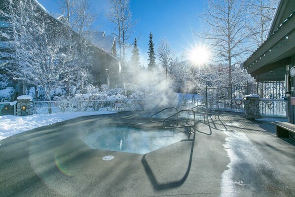 Relax in a serene hot tub surrounded by snow-covered trees and a stone wall.