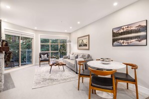 Relax in a spacious living room with a sofa, chairs, and a dining table, offering a view of lush greenery.