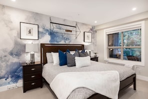 Relax in a serene bedroom with a large bed, nightstand, and window offering a view of the outdoors.