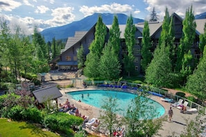 Un complex turístic amb una gran piscina envoltada d'arbres i muntanyes al fons.