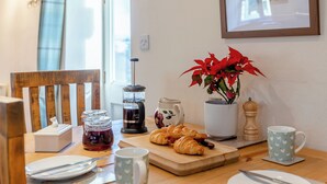 Una mesa de madera con cafetera, croissants, un florero y una taza.