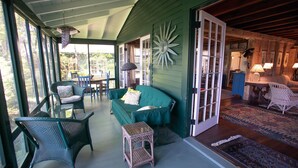 Eine gemütliche Veranda mit Korbmöbeln, einem grünen Sofa und einer dekorativen Wandverzierung im Sonnenstrahl-Design.