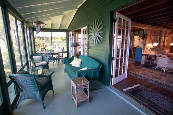 A cozy porch with wicker furniture, a green sofa, and a decorative sunburst wall piece. - Family Retreat on Squam Lake, Tennis, Kayaks, Paddleboards, Dock. (Moultonborough)