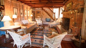 Ein gemütliches Blockhaus-Interieur mit Kamin, Korbsesseln, einer Couch und einem Bücherregal.