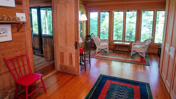 Ein Holzinterieur mit einem roten Sessel, Korbstühlen und einem Teppich.
